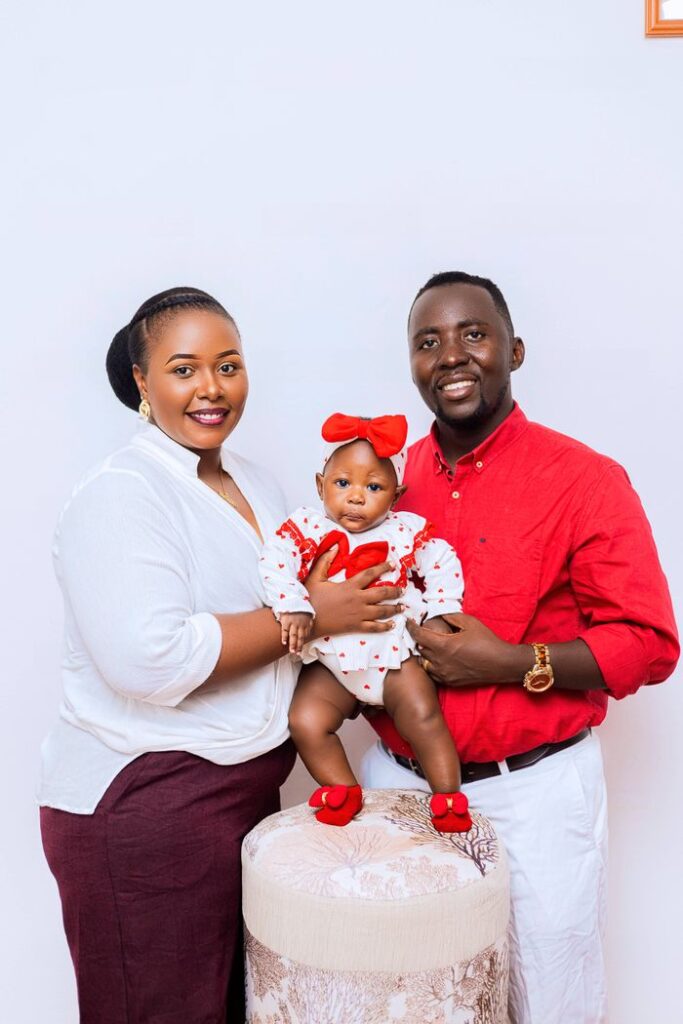 A joyful family portrait featuring a smiling couple with their baby dressed in red.