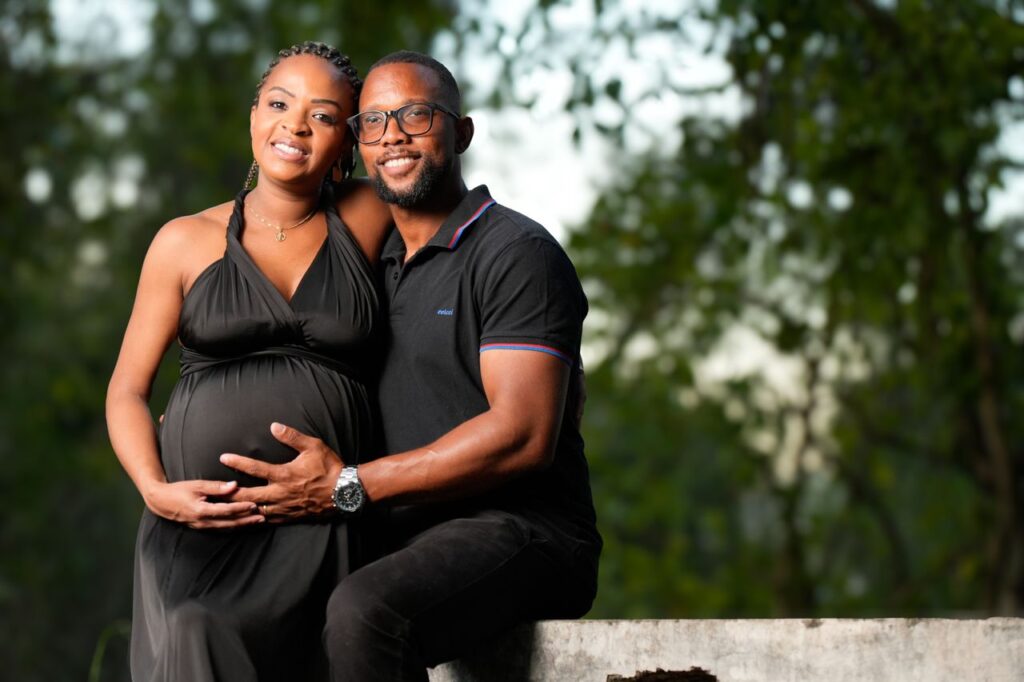Smiling couple lovingly embracing each other during pregnancy in an outdoor setting.